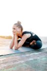 Повна форма жіночого одягу в спортивному лаві практикує Ардха Падмасану і торкається обличчя під час тренування йоги на заході сонця. — стокове фото