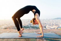Side view of young barefoot female in sportswear standing in Urdhva Dhanurasana pose while looking down during yoga practice in city — Stock Photo