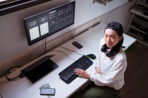 Высокоугловая азиатская женщина, работающая на компьютере с графиками, демонстрирующими динамику изменения стоимости криптовалют на удобном рабочем месте — стоковое фото