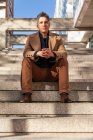 Selbstbewusster seriöser Geschäftsmann im formellen Anzug sitzt auf der Treppe und blickt in die Kamera — Stockfoto