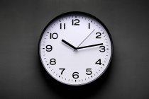 Reloj minimalista de forma redonda con números y flechas sobre fondo negro - foto de stock