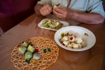 Cropped unrecognizable senior male with knife peeling green fig at table with disposable tray in house room — Stock Photo
