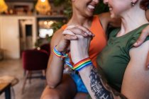 Cheerful cropped unrecognizable young tattooed woman embracing lesbian girlfriend while looking at each other on couch in house — Stock Photo