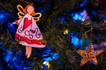 Angel and star shaped decorations hanging on branches of artificial Christmas fir tree glowing at night — Stock Photo