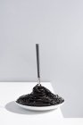 Edelstahl-Gabel in voller Schüssel mit schwarzen Spaghetti mit Tintenfischtinte auf weißem Tisch im Studio auf grauem Hintergrund — Stockfoto