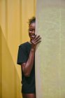 Весела молода афроамериканська спортсменка у бікіні та футболці, яка дивиться на камеру з дошкою у жовтому контейнері на узбережжі. — стокове фото