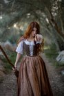 Mystische Hexe in Kleid und mit Besenstiel, die im dunklen Wald im Herbst auf die Kamera zeigt — Stockfoto
