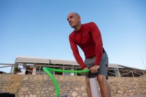 Снизу мужчина-серфер в гидрокостюме накачивает доску SUP, стоя на берегу моря и готовится к серфингу — стоковое фото