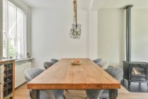 Tavolo in legno e comode sedie grigie posizionate vicino al camino in sala da pranzo in appartamento durante il giorno — Foto stock