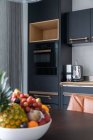Schüssel mit frischen Früchten auf Holztisch in zeitgenössischer Küche mit minimalistischen schwarzen Möbeln bei Tageslicht — Stockfoto