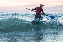 Rückenansicht eines nicht wiederzuerkennenden männlichen Surfers in Neoprenanzug und Hut auf dem Paddelbrett beim Surfen am Strand — Stockfoto