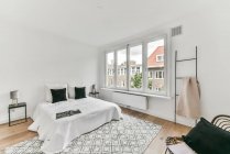 Comodo letto rivestito con copriletto bianco posto su moquette vicino alla finestra in elegante camera da letto — Foto stock