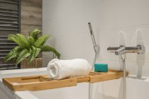 Toalla blanca en estante de madera en la bañera llena de agua en el baño con paredes de azulejos - foto de stock