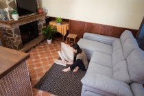 Mesa de montaje femenina étnica atenta joven en alfombra ornamental contra sofá en la sala de casa de luz - foto de stock