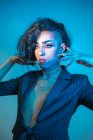 Молодой транссексуал модель с макияжем в стильной куртке глядя в сторону на синем фоне — стоковое фото