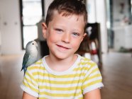 Carino bambino in maglietta a righe seduto con uccellino con piumaggio grigio a casa — Foto stock