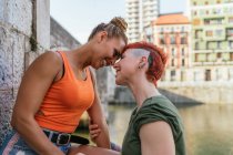 Seitenansicht einer fröhlichen jungen homosexuellen Frau, die tätowierte Freundin mit Mohawk umarmt, während sie sich am Kanal in der Stadt anschaut — Stockfoto