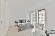 Інтер'єр просторої світлої спальні зі зручним ліжком і великими вікнами в сучасній квартирі вдень — стокове фото