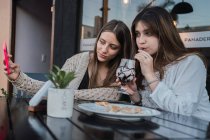 Migliori amiche con bicchieri di bevande rinfrescanti scattare autoritratto sul cellulare a tavola in caffè urbano — Foto stock
