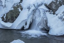 Lange Belichtung des schnellen Wasserfalls, der durch schneebedecktes Gelände im Sierra de Guadarrama Nationalpark fließt — Stockfoto