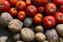 Vista superior close-up de uma pilha de tomates vermelhos e batatas no chão — Fotografia de Stock
