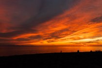 Вид на туристичні силуети, що захоплюють нескінченний океан з берега під хмарним небом з блискучим сонцем в сутінках — стокове фото