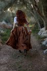 Обратный вид неузнаваемой ведьмы в одежде и с метлой, бегущей по тропинке в осеннем лесу — стоковое фото