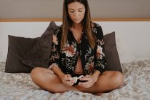 Expectant female in underwear sitting with crossed legs while looking to baby socks sitting on soft bed in house — Stock Photo