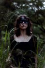Bruxa mística em vestido preto longo e com rosto pintado de pé olhando para longe em madeiras sombrias escuras — Fotografia de Stock