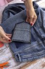 Dall'alto di coltura femminile irriconoscibile con manicure che fissa la tasca di jeans su tavolo in camera leggera — Foto stock