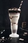 Milkshake savoureux avec biscuits écrasés et paille en verre avec sauce au chocolat — Photo de stock