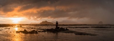 Silhouette di viaggiatore femminile in piedi su rocce di mare con colline sotto cielo nuvoloso e luce solare brillante in Malesia — Foto stock