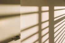 Intérieur de la poignée de porte dans le couloir loft spacieux vide avec des ombres géométriques et la lumière du soleil sur les murs blancs — Photo de stock