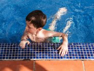 Deleitado niño lindo con el pelo mojado apoyado en la piscina mientras se divierten durante el fin de semana de verano - foto de stock