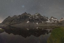 Malerische Landschaft hoher felsiger Berge, bedeckt mit Schnee, der sich im ruhigen Wasser des Flusses unter dem Sternenhimmel spiegelt — Stockfoto