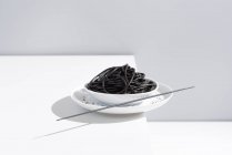 Von oben Keramikschale mit leckeren Spaghetti mit schwarzer Tintenfischtinte mit Essstäbchen auf grauem Hintergrund — Stockfoto