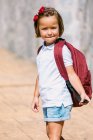 Side view of schoolchild with backpack on pavement looking at camera in sunlight — Stock Photo