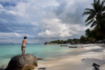 Vista posterior cuerpo completo de mujer turista descalza en traje de baño de pie en la roca y admirar el mar azul durante las vacaciones en Malasia - foto de stock