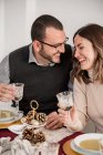 Возделывайте веселую пару с бокалами алкогольного напитка, взаимодействуя, смеясь за столом со сливочными супами во время новогодних праздников — стоковое фото