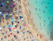 Drone vista de los viajeros en la costa arenosa de Ibiza contra el mar ondulado a la luz del sol en España - foto de stock