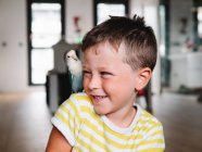 Симпатичний маленький хлопчик в смугастій сорочці, що сидить з маленькою пташкою з сірим оперенням вдома — стокове фото