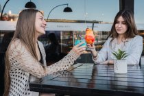 Fröhliche Teenagerinnen interagieren beim Gläschen mit köstlichen Erfrischungsgetränken am Tisch in der städtischen Cafeteria — Stockfoto