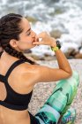 Vista laterale di atleta donna magra in abbigliamento sportivo seduta sul lungomare di pietra vicino al mare e dopo aver interrotto durante l'allenamento — Foto stock