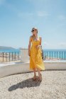 Feminino viajante de vestido em pé perto de cerca e admirando cidade costeira velha durante as férias de verão — Fotografia de Stock