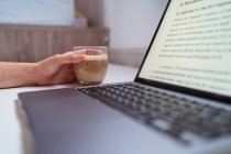 Обрезанная неузнаваемая женщина-блоггер за столом с нетбуком и кофе — стоковое фото