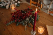 From above of festive Christmas bouquet with branches of cotton, fir and twigs of eucalyptus and bright red branches with berries placed on wooden table with candles in room — Stock Photo