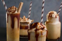 Разнообразные стаканы со сладким карамельным молочным коктейлем с ванильным мороженым и вафельным печеньем подаются на столе — стоковое фото