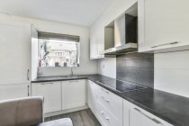 Сучасний інтер'єр кухні з білими шафами і побутовою технікою в квартирі, спроектованій в мінімальному стилі — стокове фото