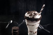Вкусный молочный коктейль с измельченным печеньем и соломой в стакане с шоколадным соусом — стоковое фото
