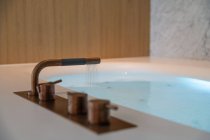 Interno del bagno contemporaneo con vasca idromassaggio con acqua pulita contro la parete luminosa in appartamento — Foto stock